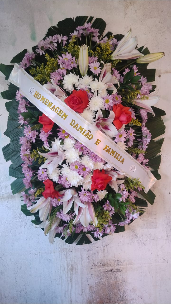 coroa de flores fúnebre com rosas vermelhas, lírios e margaridas roxas e brancas com faixa dourada pendurada n